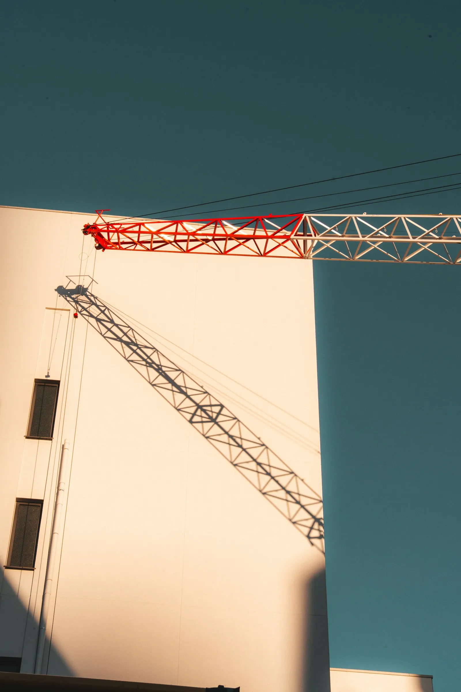 Grue de chantier et son ombre projetée sur une façade blanche, ciel bleu